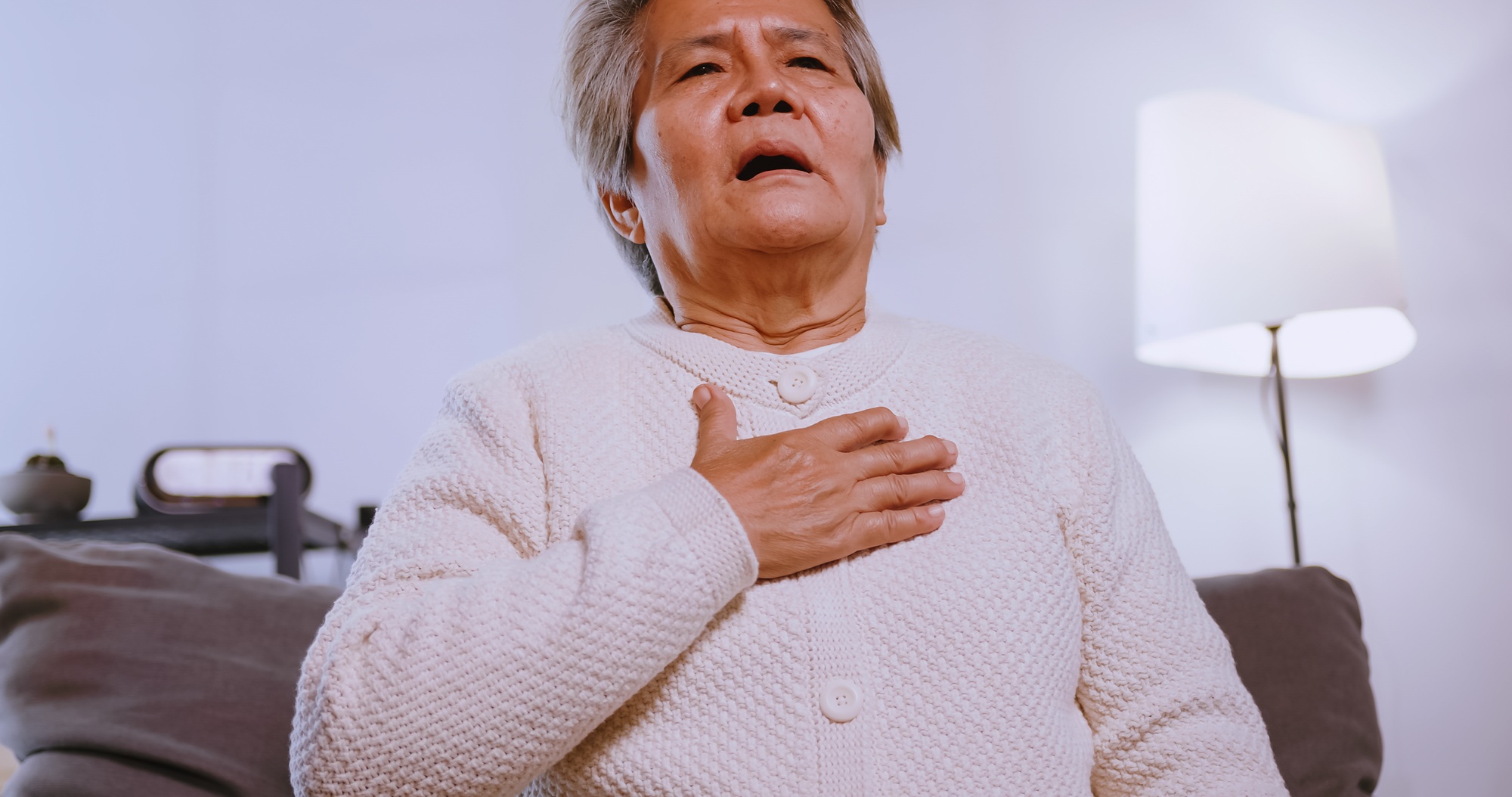 Asian old woman having difficulty breathing while sitting on the sofa at home.